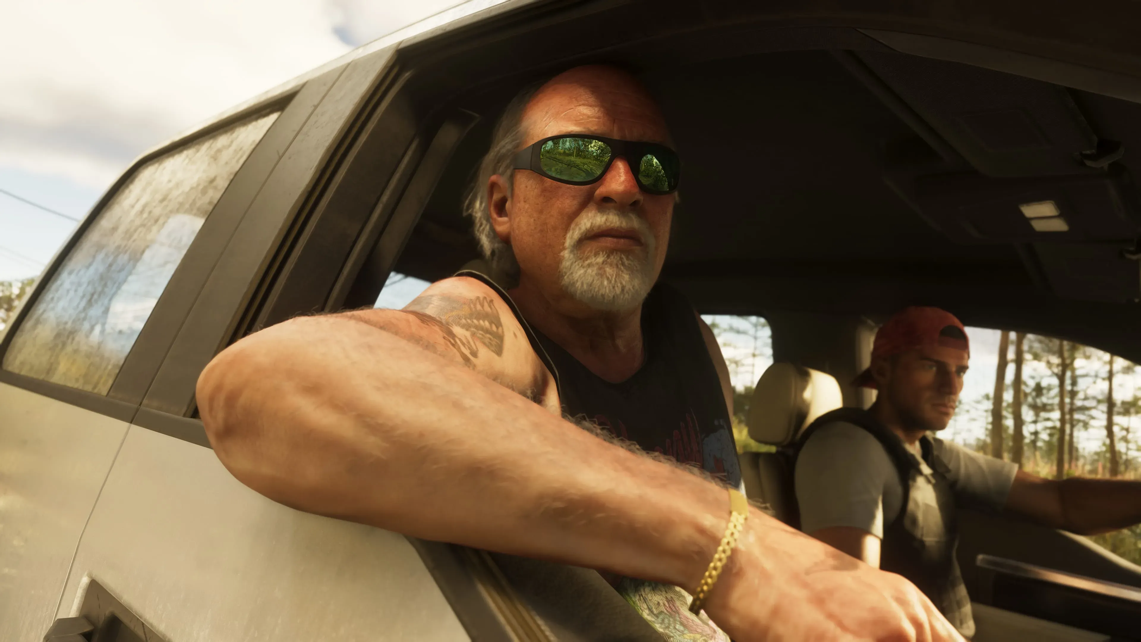 Dois homens dentro de um carro, com o mais velho de óculos escuros encostado na janela e o mais jovem dirigindo, em um ambiente ensolarado e arborizado.